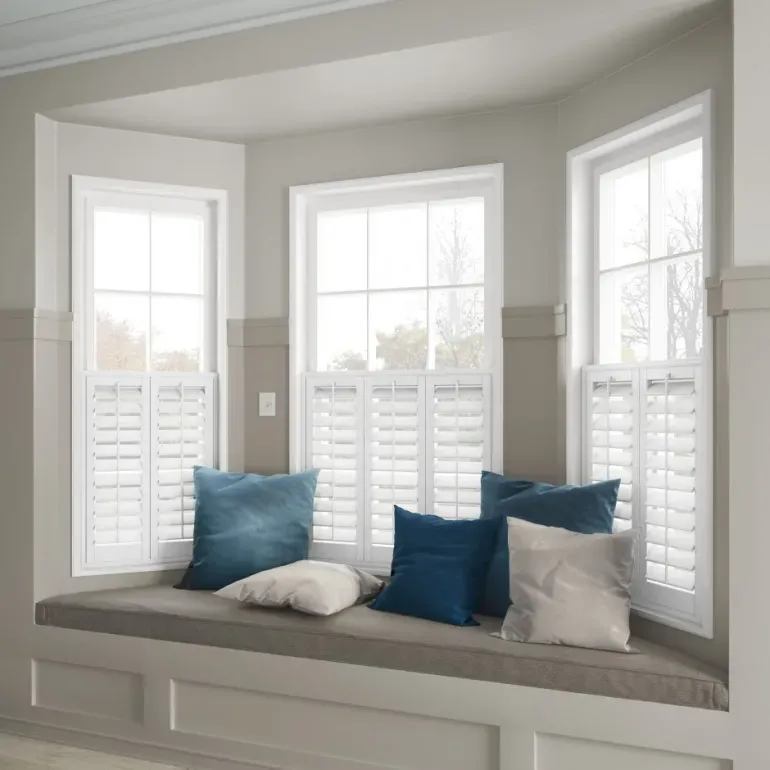 White café-style plantation shutters fitted on bay windows with a built-in window seat and cushions – perfect for light control and privacy, supplied by Material Things in Hampshire.