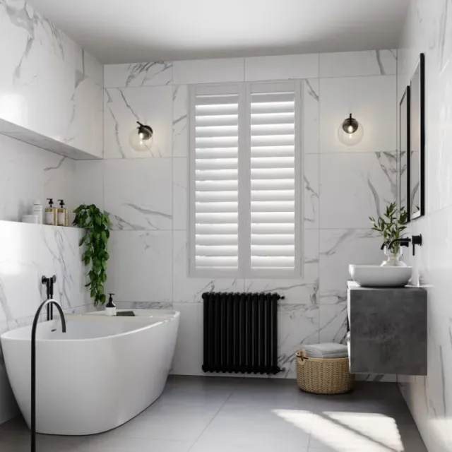 Modern bathroom with full-height white window shutters, marble-effect walls, freestanding bath, and minimalist black fittings.