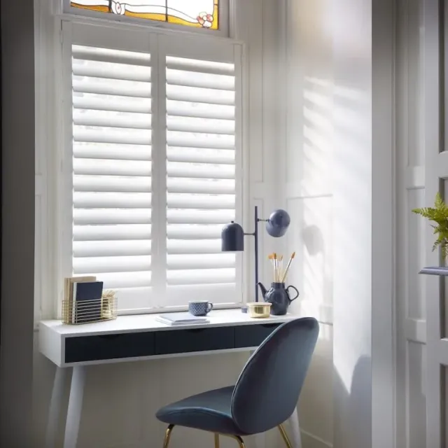 White window shutters in a bright home office space, filtering natural light and adding privacy to a stylish modern interior.
